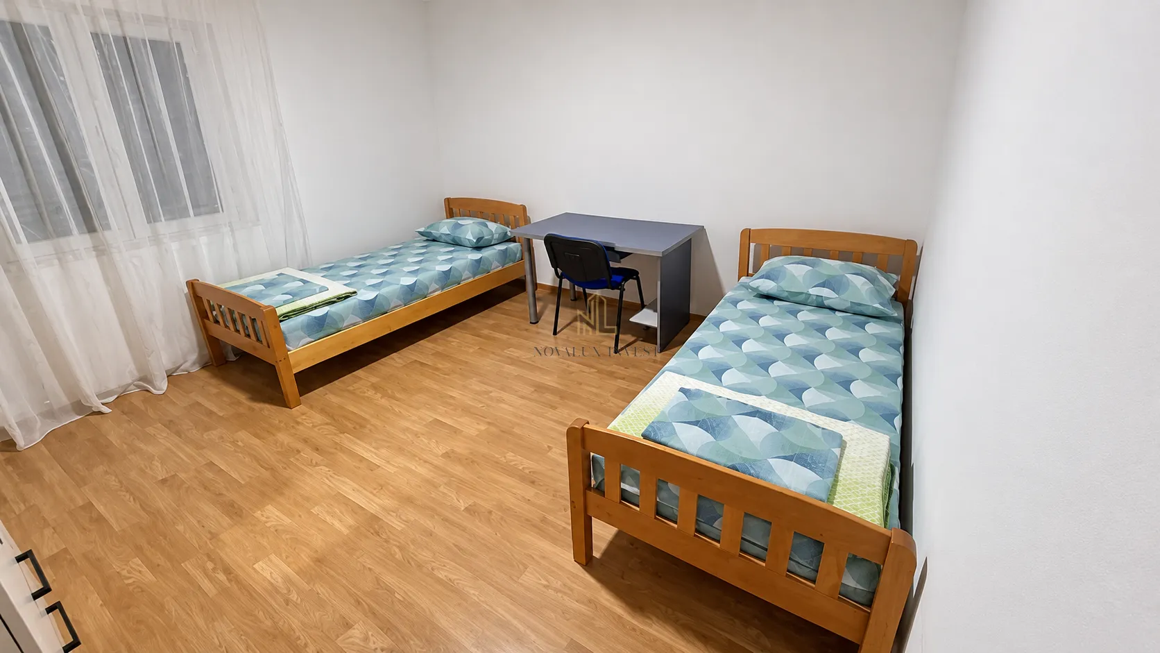 Spavaća soba sa dva drvena kreveta na spuštanje i radnim stolom.