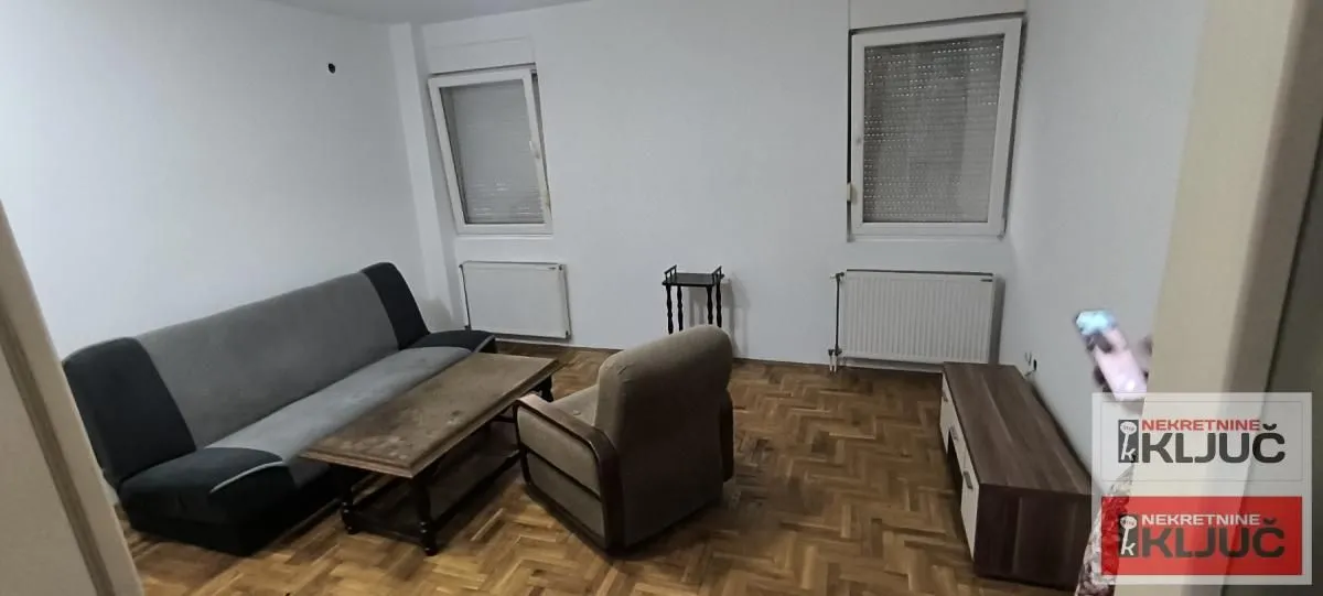 Dnevna soba sa garniturom za sedenje i drvenim parketom.