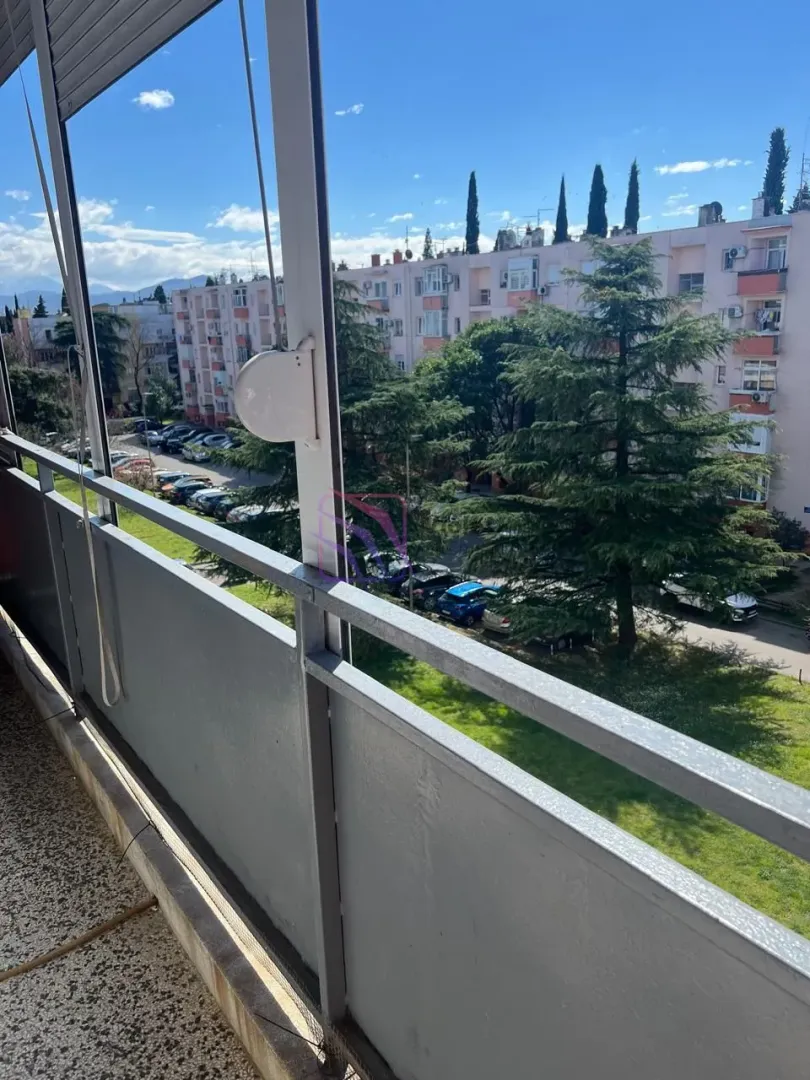 Pogled sa balkona na okolne zgrade i zelenu površinu sa drvećem.