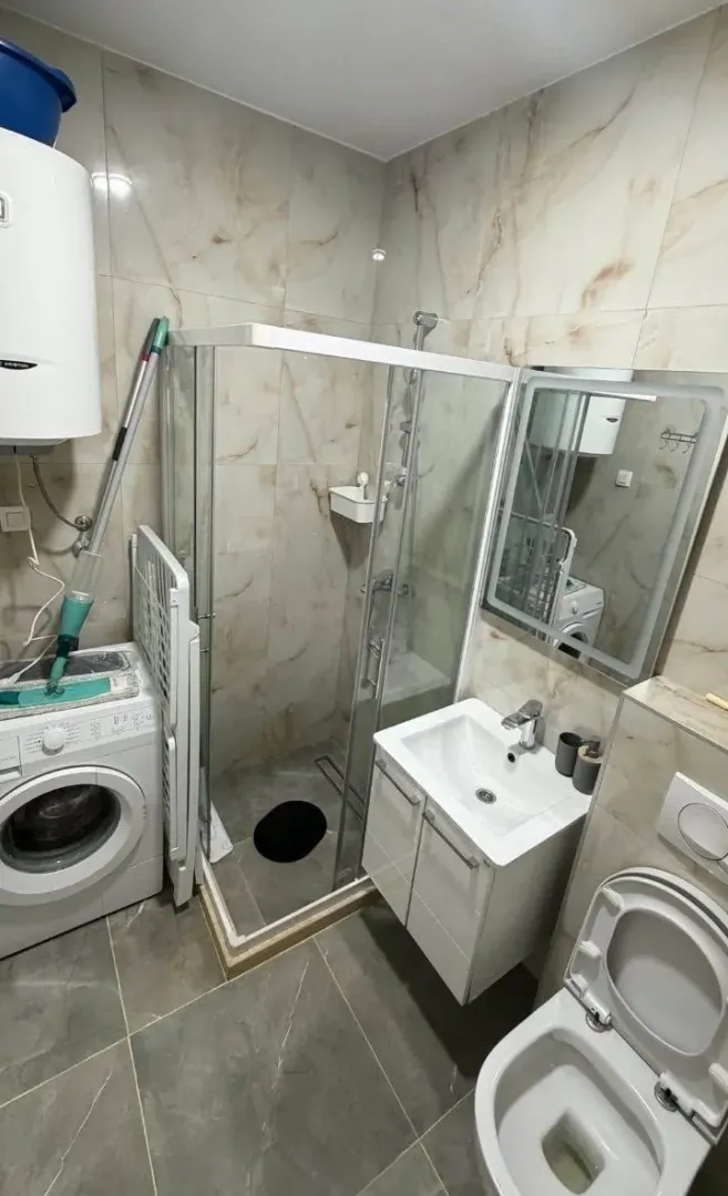 Manje opremljeno kupatilo sa tuš kabinom, umivaonikom i veš mašinom.