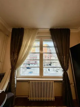 View through a window with curtains looking out at the city street and buildings. - image 14