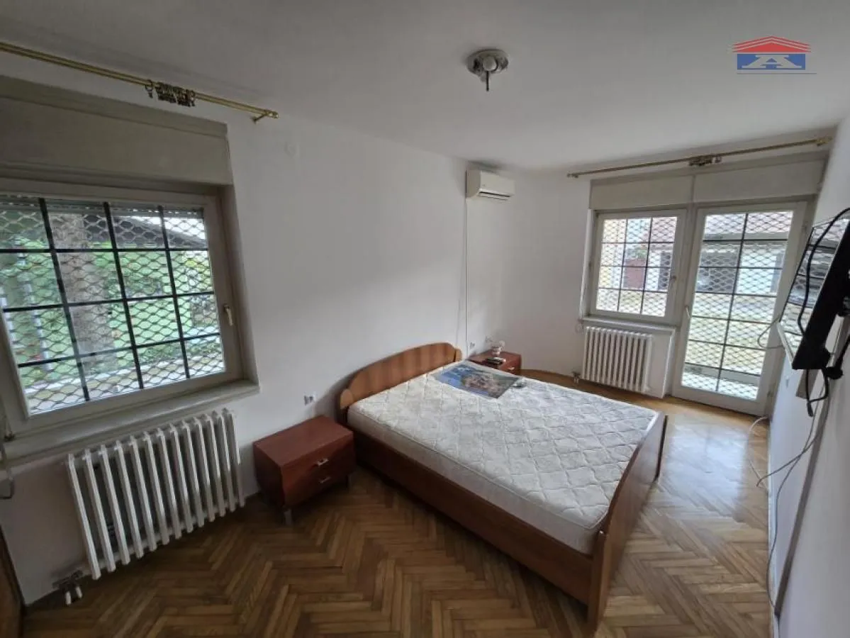 Bedroom with a double bed, wooden flooring and two windows.