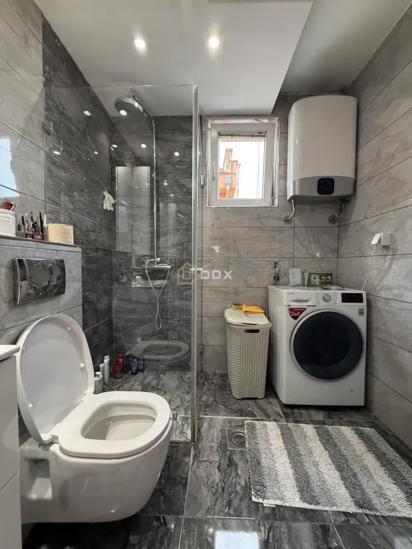 Moderno opremljeno kupatilo sa tuš kabinom i veš mašinom.