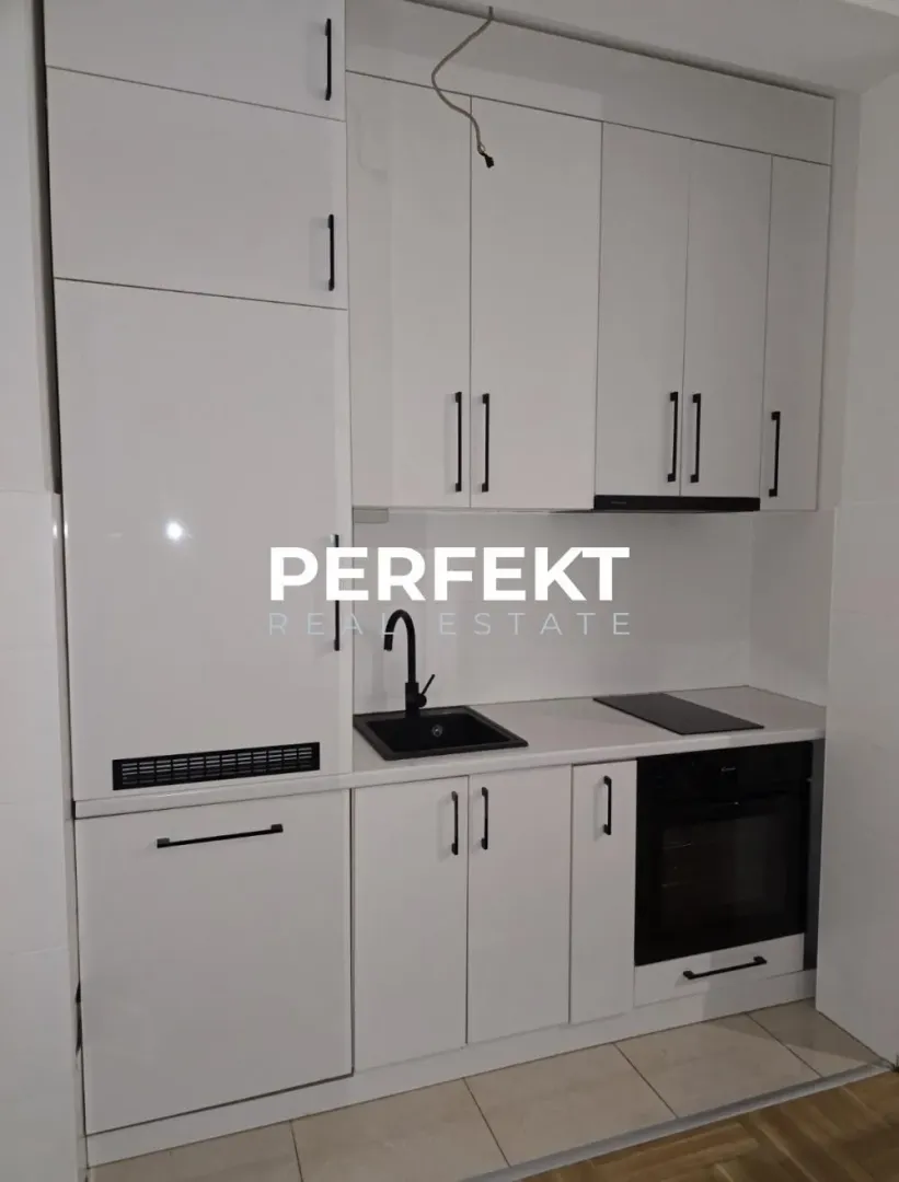 Manja bela kuhinja sa crnim detaljima i ugradnim aparatima.