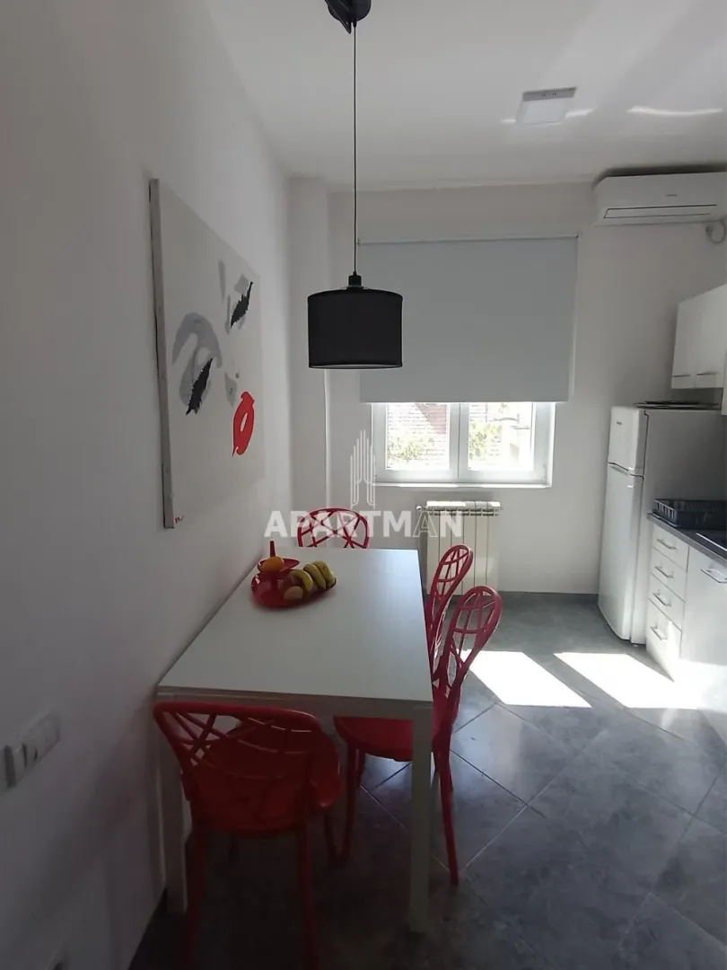 Trpezarija sa belim stolom i crvenim stolicama pored kuhinje.