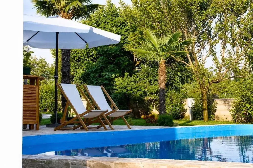 Yard with a swimming pool, sun loungers and an umbrella.