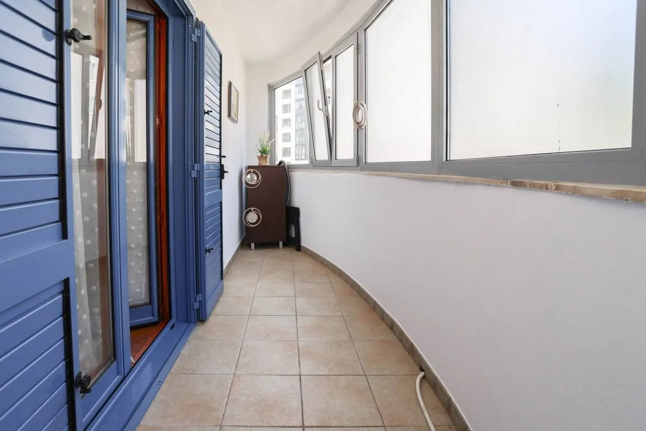 Enclosed balcony with tiled flooring and blue shutters.
