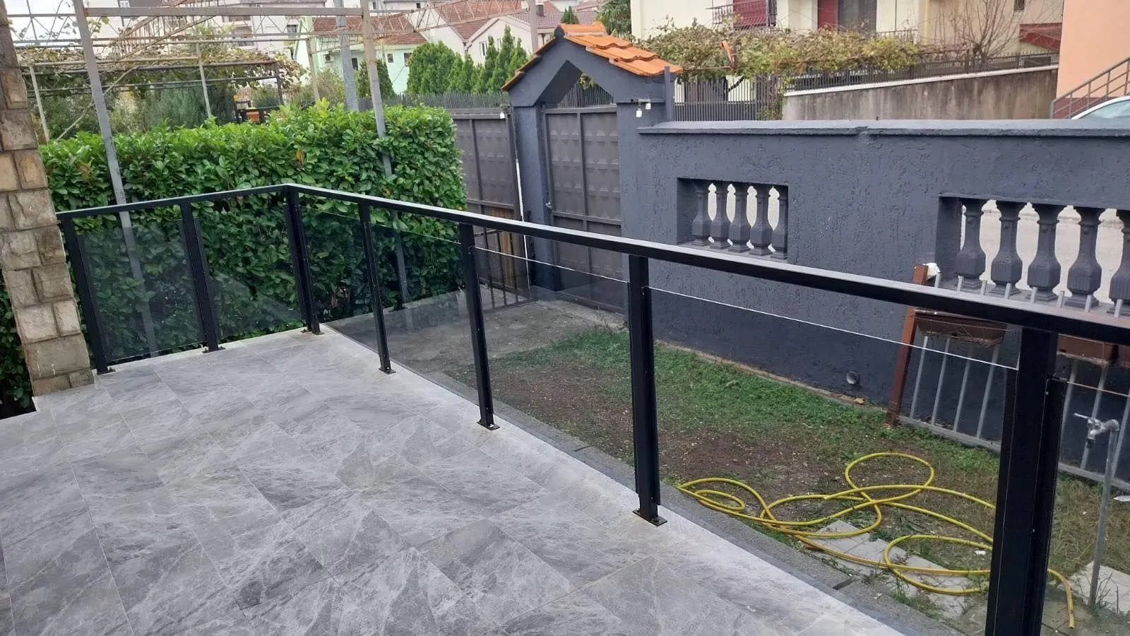 Popločana terasa sa modernom staklenom ogradom i pogledom na dvorište.