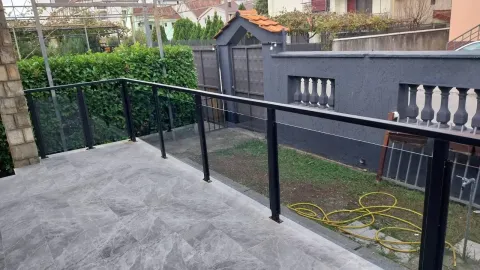 Popločana terasa sa modernom staklenom ogradom i pogledom na dvorište. - image 7