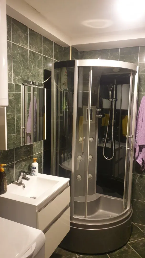 Kupatilo sa modernom tuš kabinom, lavaboom i zelenim pločicama.