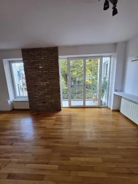 Prazna dnevna soba sa drvenim podom, ciglenim stubom i izlazom na terasu. - image 6