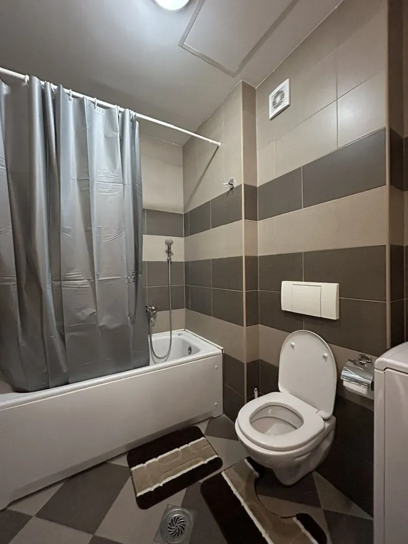 Kupatilo sa kadom, toaletom i pločicama u sivo-braon tonovima.