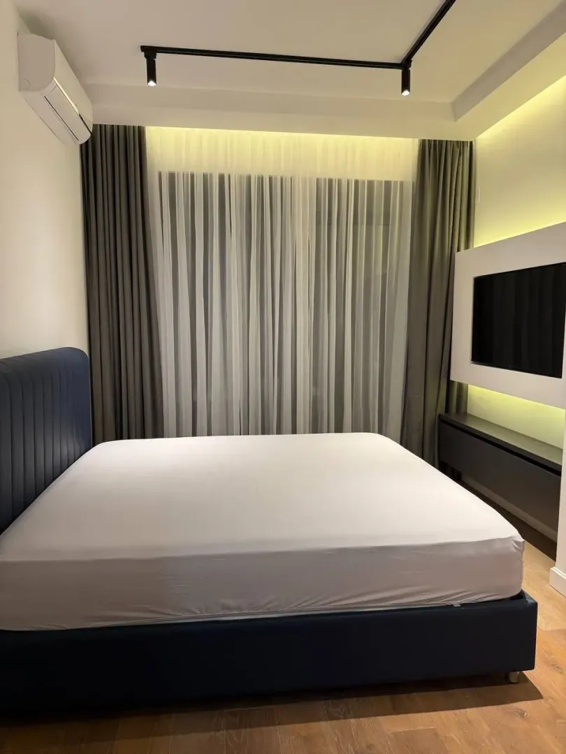 Modern bedroom with a double bed, TV, and curtains.