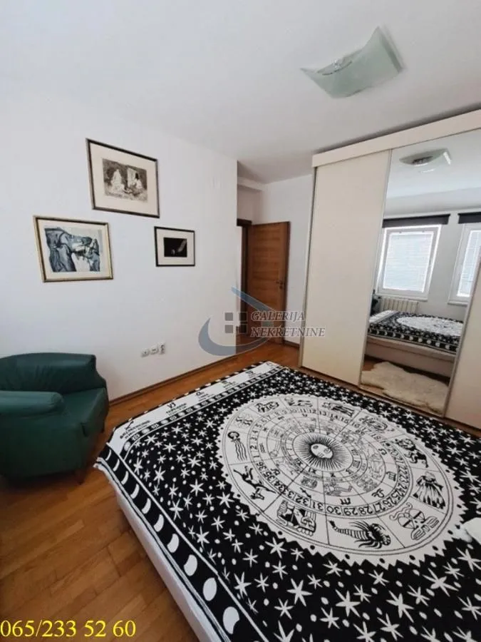 Nameštena spavaća soba sa bračnim krevetom, velikim plakarom i foteljom.