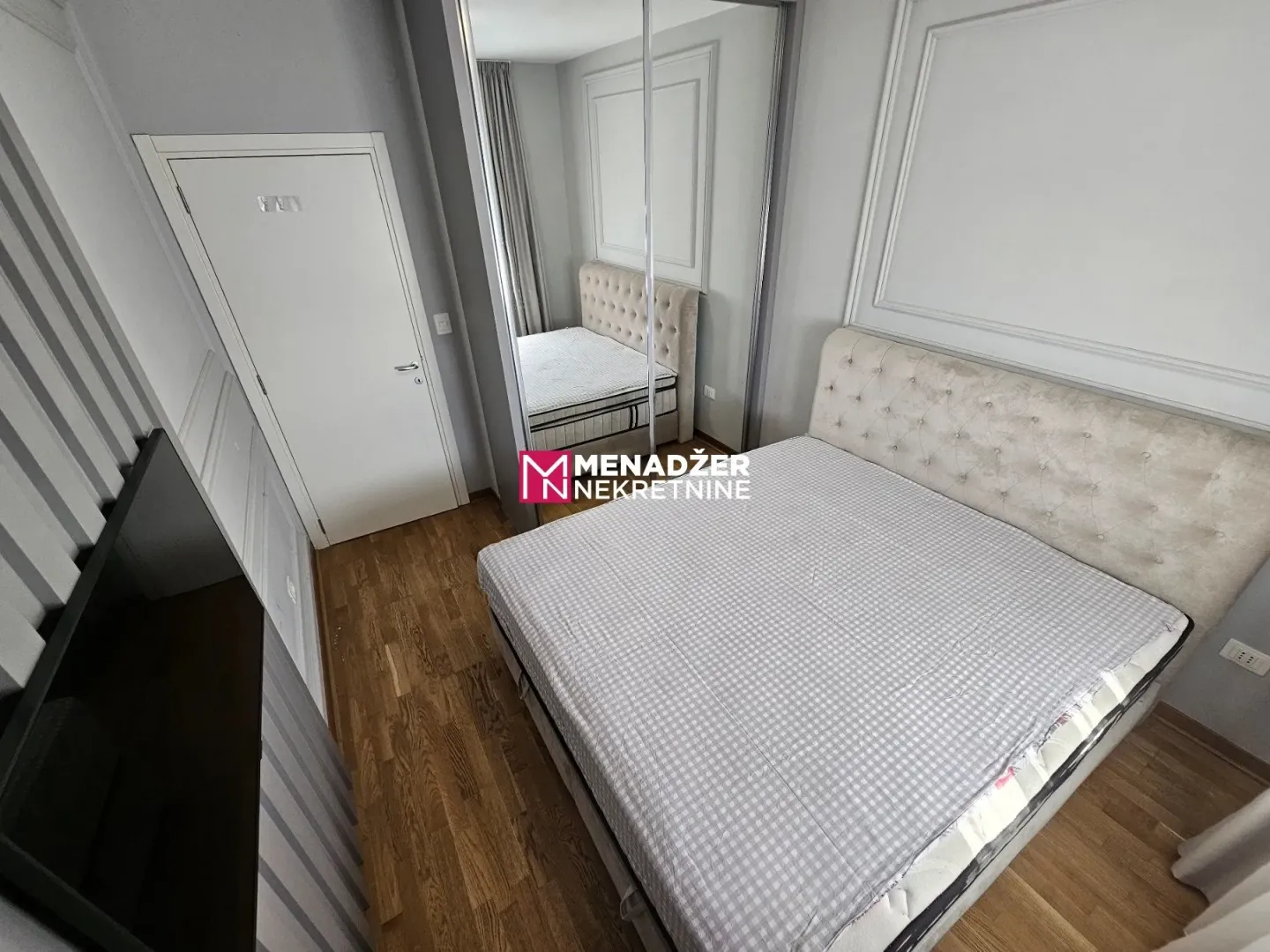 Modern bedroom with a double bed, wooden flooring, and a mirrored built-in wardrobe.