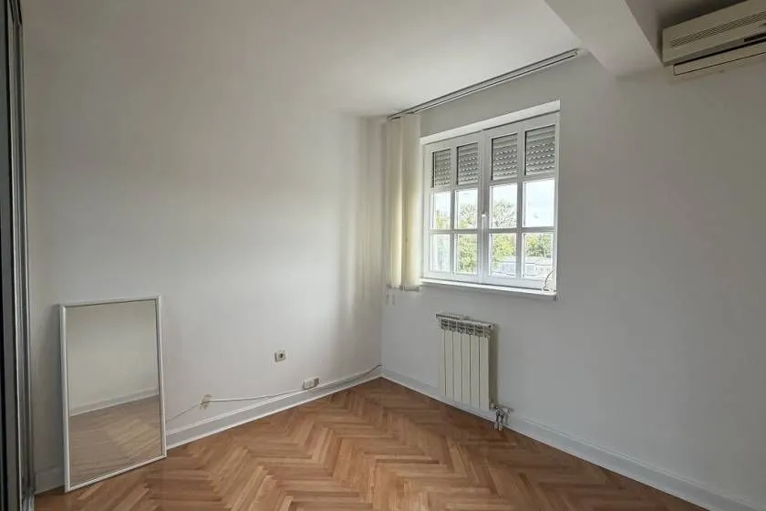 Prazna soba sa prozorom, parketom na podu i ogledalom.