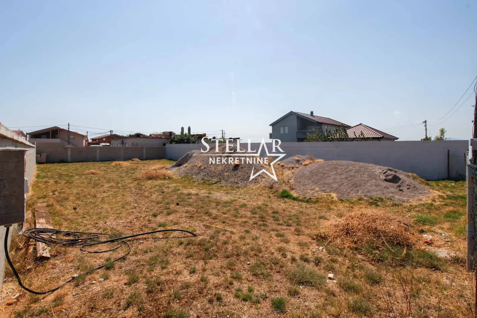 Pogled na ograđeno dvorište sa gomilama građevinskog materijala.