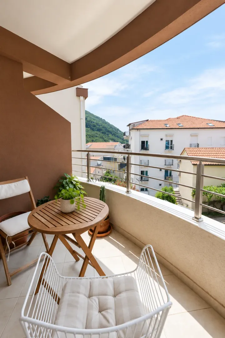 Namješten balkon sa stolom, stolicama i pogledom na okolne zgrade i brda.