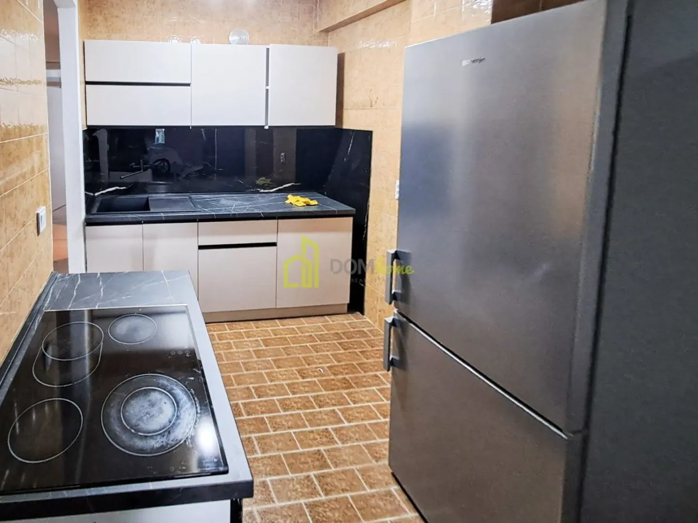 Kitchen equipped with white cabinets, a refrigerator, and a black countertop with a built-in hob.