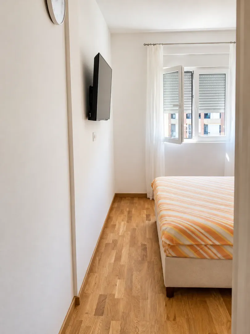 Small bedroom with a bed, wooden flooring, and a window.
