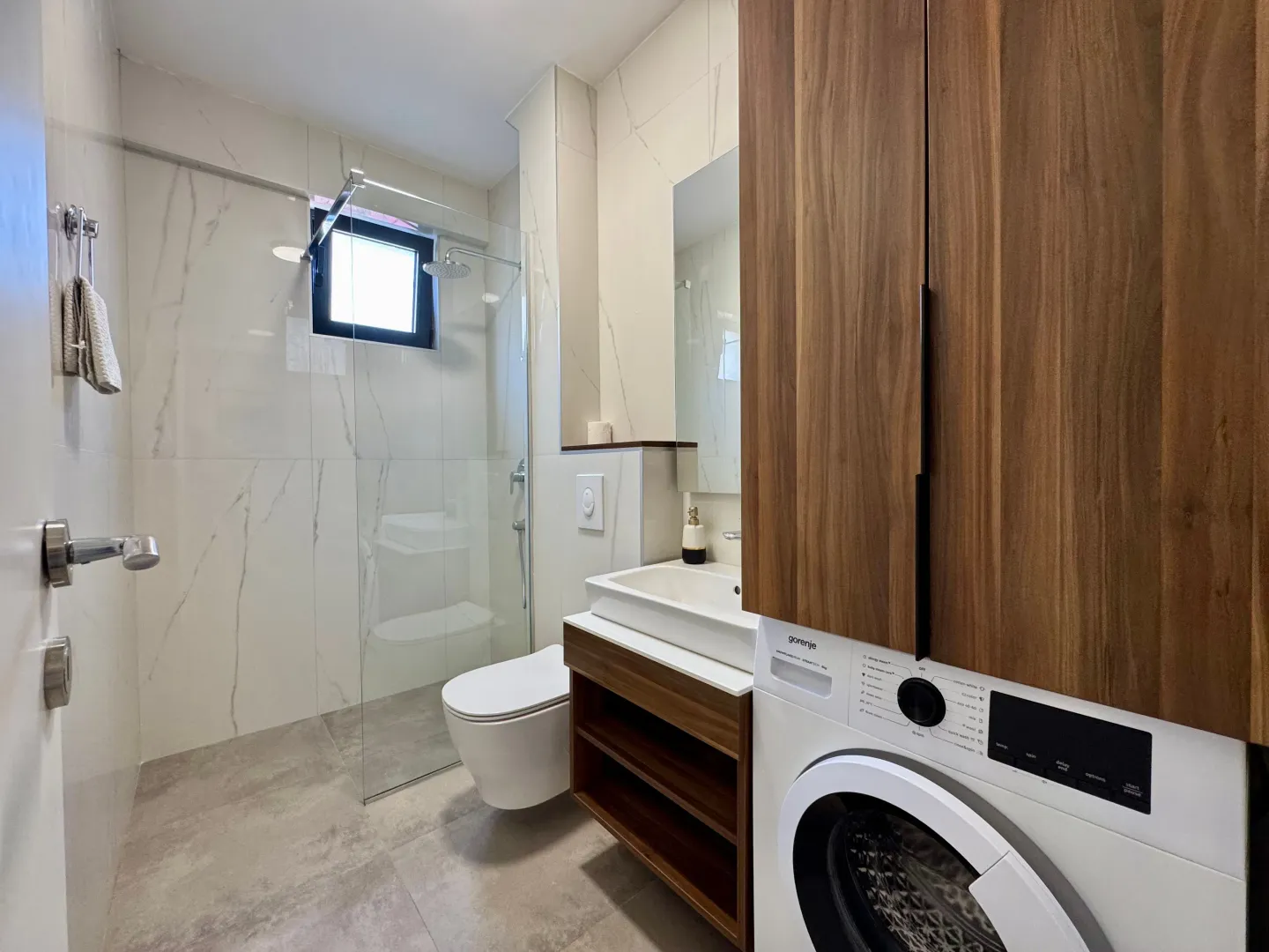 Modern bathroom equipped with a walk-in shower, washbasin, and washing machine.