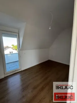 Prazna soba sa kosim plafonom, drvenim podom i izlazom na terasu. - image 3