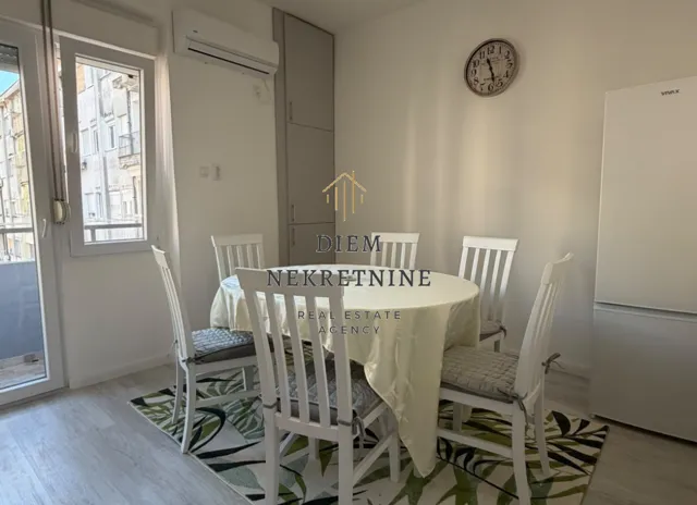 Dining area with a table, chairs, and a refrigerator in light tones.