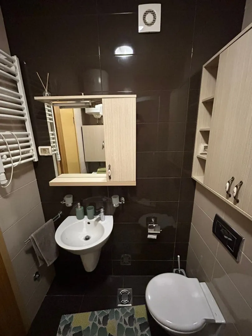 Small bathroom with a washbasin, mirror, toilet, and wall cabinets.