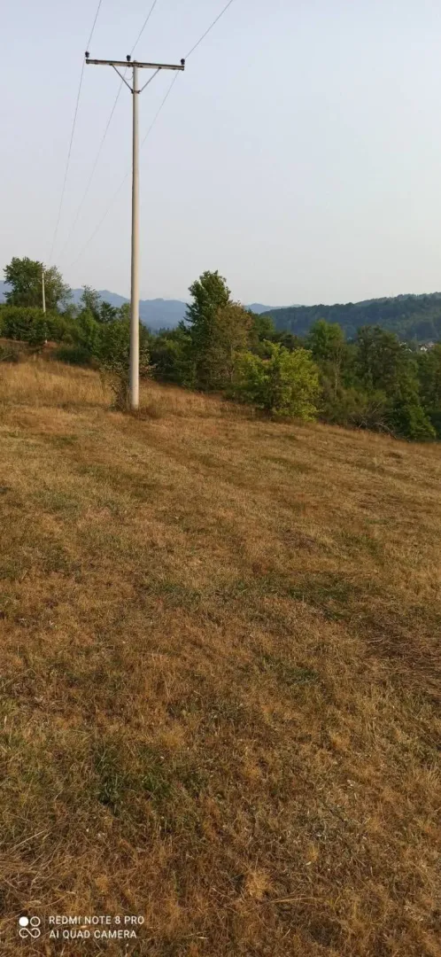 Travnati plac sa dalekovodom i pogledom na brda.