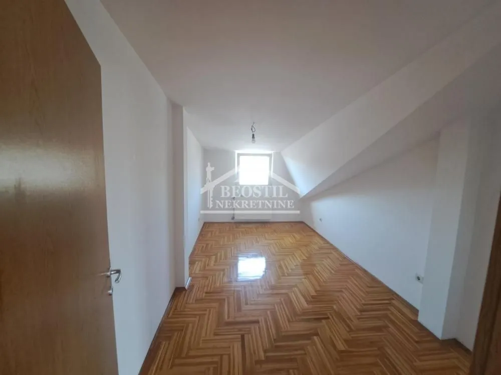 Prazna potkrovna soba sa drvenim parketom i prozorom na kraju.