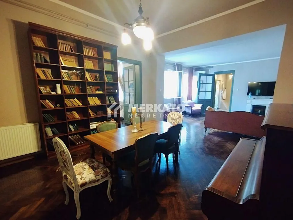 Prostrana dnevna soba sa trpezarijom, velikom bibliotekom i drvenim nameštajem.