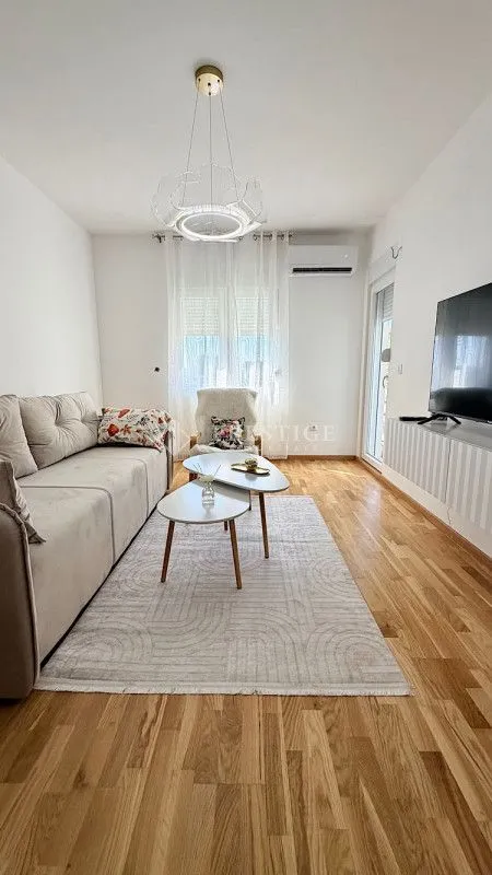 Svijetao dnevni boravak sa garniturom, drvenim podom i modernim lusterom.