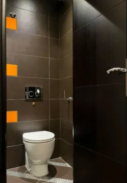 Small bathroom clad in dark tiles with orange accents and a wall-hung toilet. - image 13