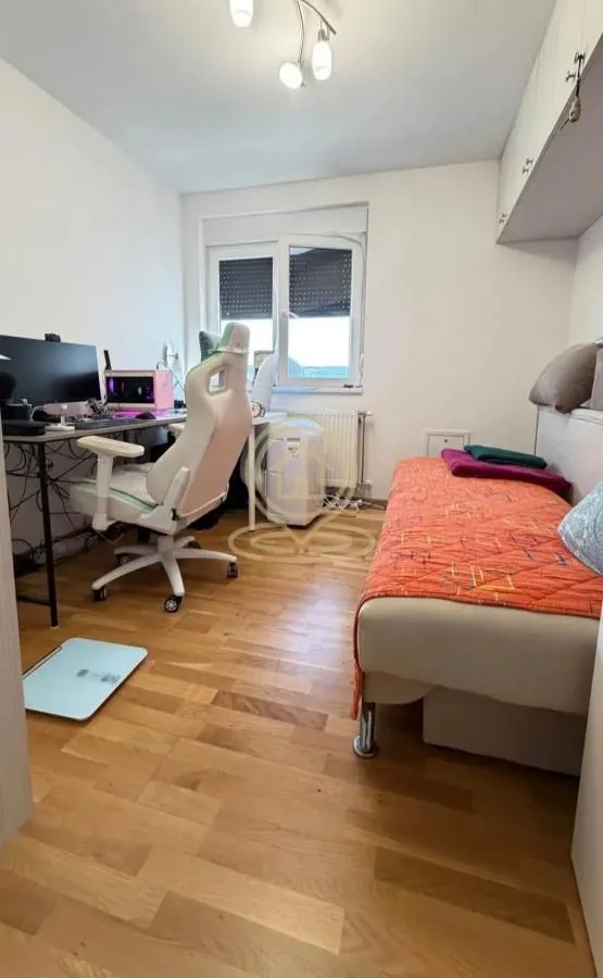 Manja spavaća soba sa krevetom, radnim stolom i računarom.
