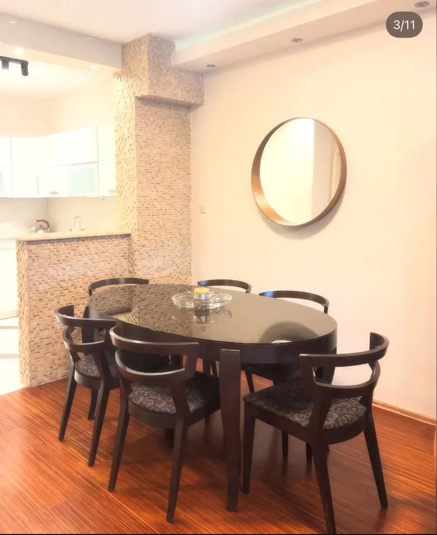Dining area with a dark table and chairs, decorated with a round wall mirror.