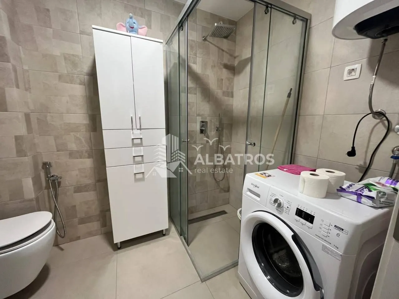 Kupatilo opremljeno tuš kabinom, WC šoljom, ormarićem i veš mašinom.