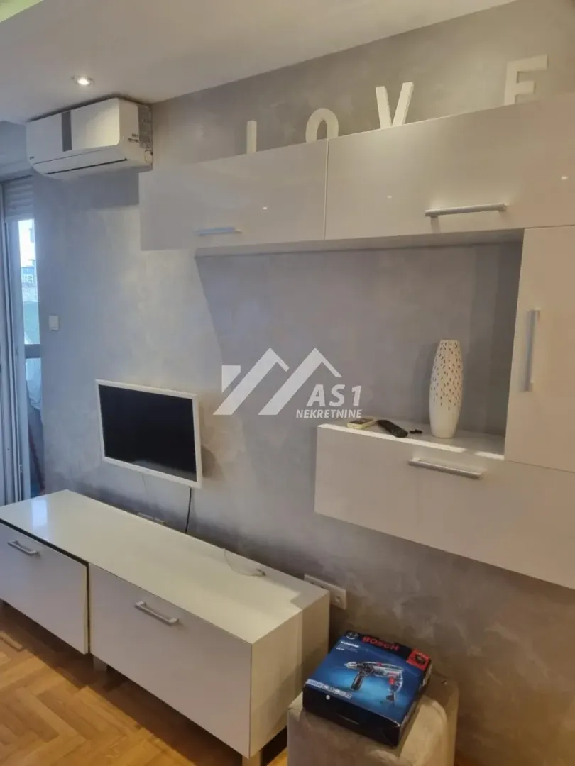 Dnevna soba sa belim nameštajem, televizorom i klima uređajem.