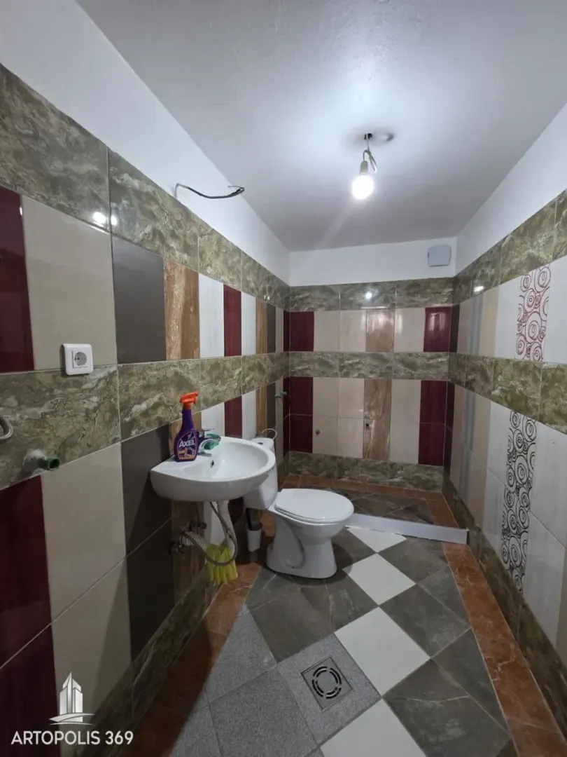 Small bathroom covered with ceramic tiles, featuring a sink and a toilet.
