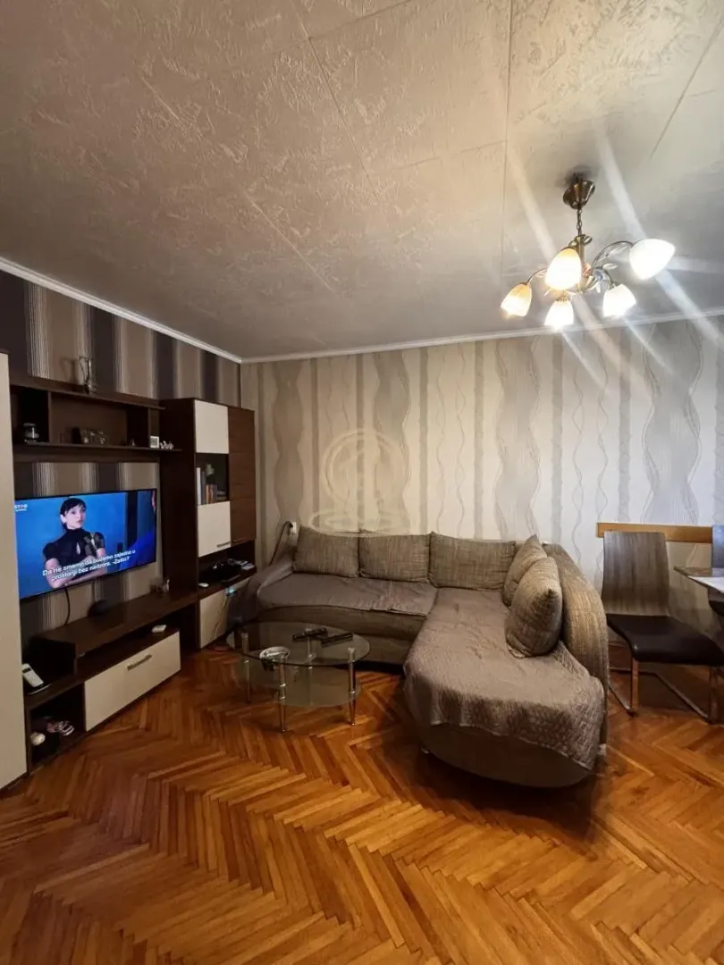 Dnevna soba sa ugaonom garniturom, televizorom i trpezarijskim stolom.