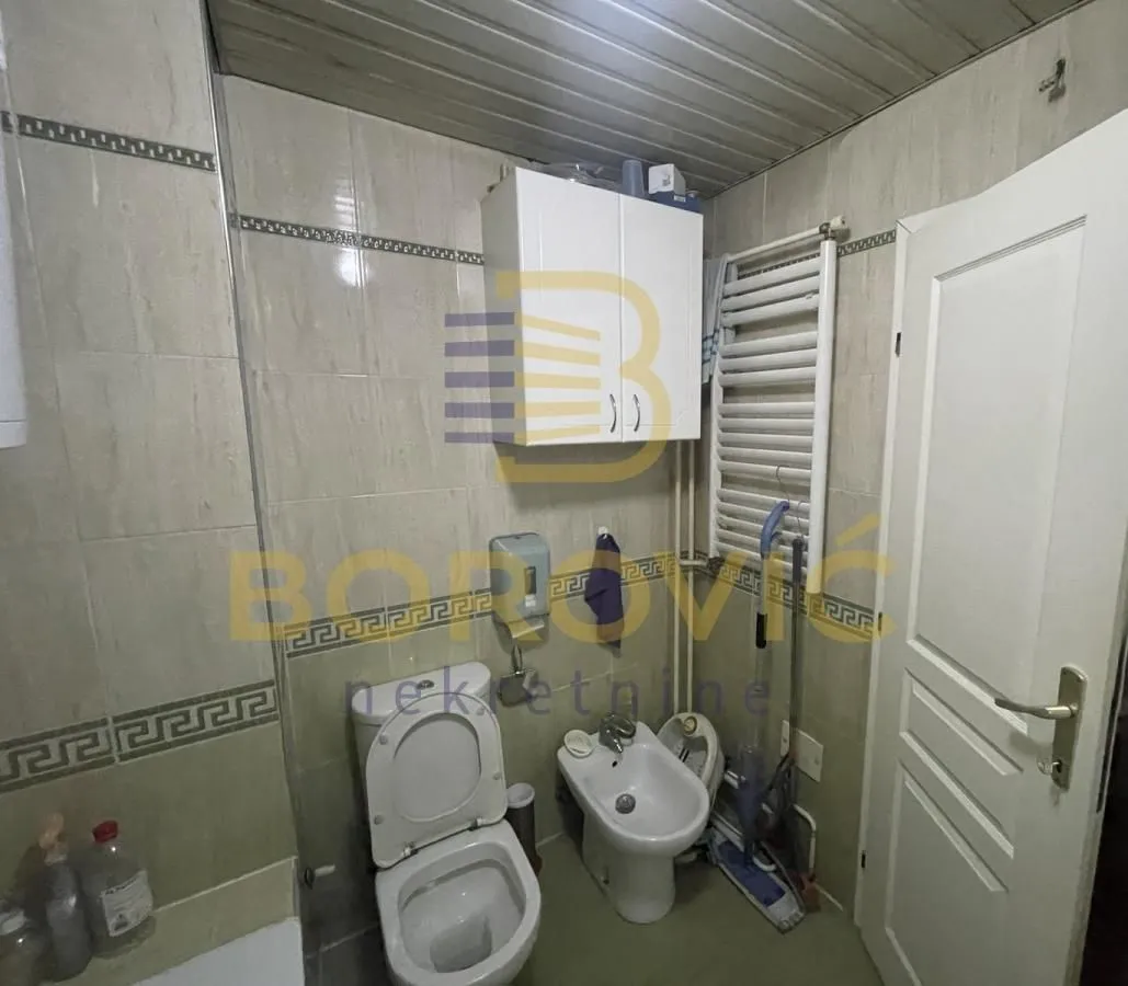 Manje kupatilo sa pločicama, wc šoljom, bideom i zidnim ormarićem.