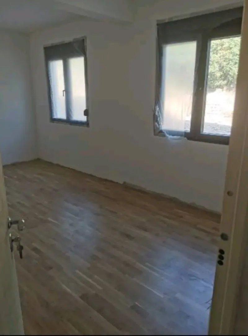 Prazna soba sa parketom i bijelim zidovima tokom renoviranja.