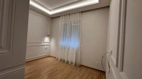 Prazna soba sa drvenim podom, dekorativnim lajsnama na zidovima i belim zavesama. - image 11