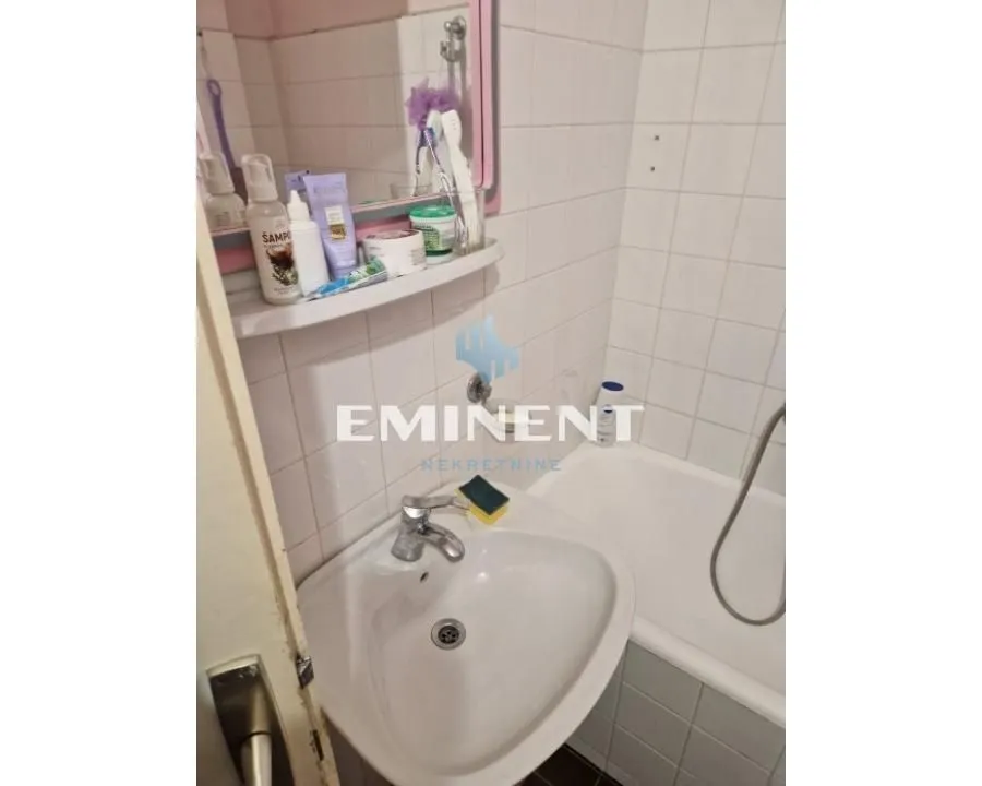 Manje kupatilo sa umivaonikom, ogledalom i kadom obloženom pločicama.