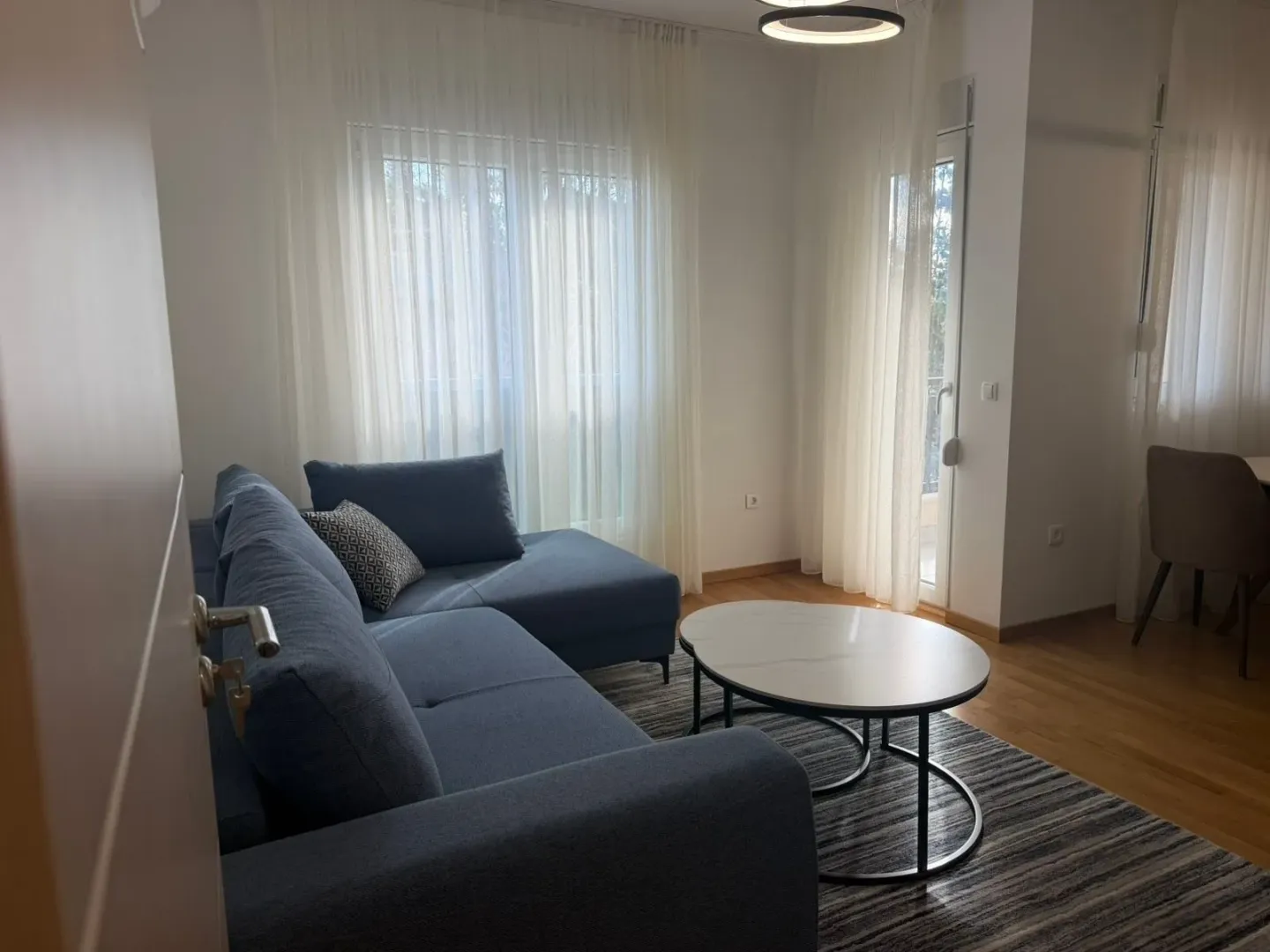 Living room with a sectional sofa, coffee table, and windows with white curtains.