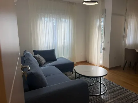 Living room with a sectional sofa, coffee table, and windows with white curtains. - image 2
