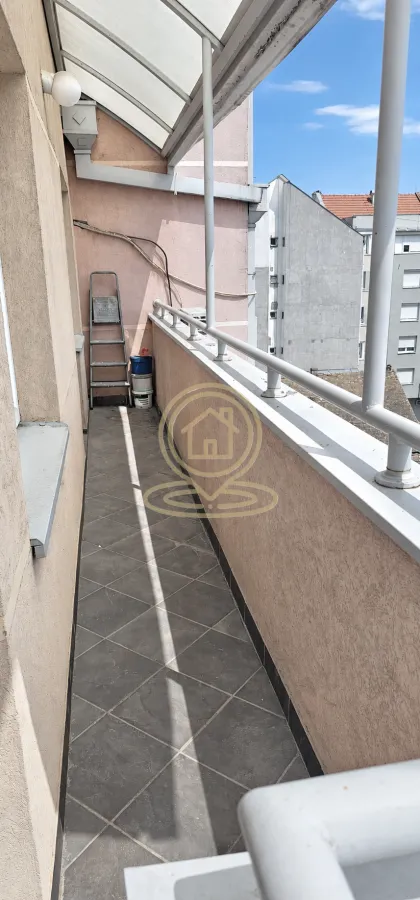 Dugi natkriveni balkon sa pločicama i metalnom ogradom.