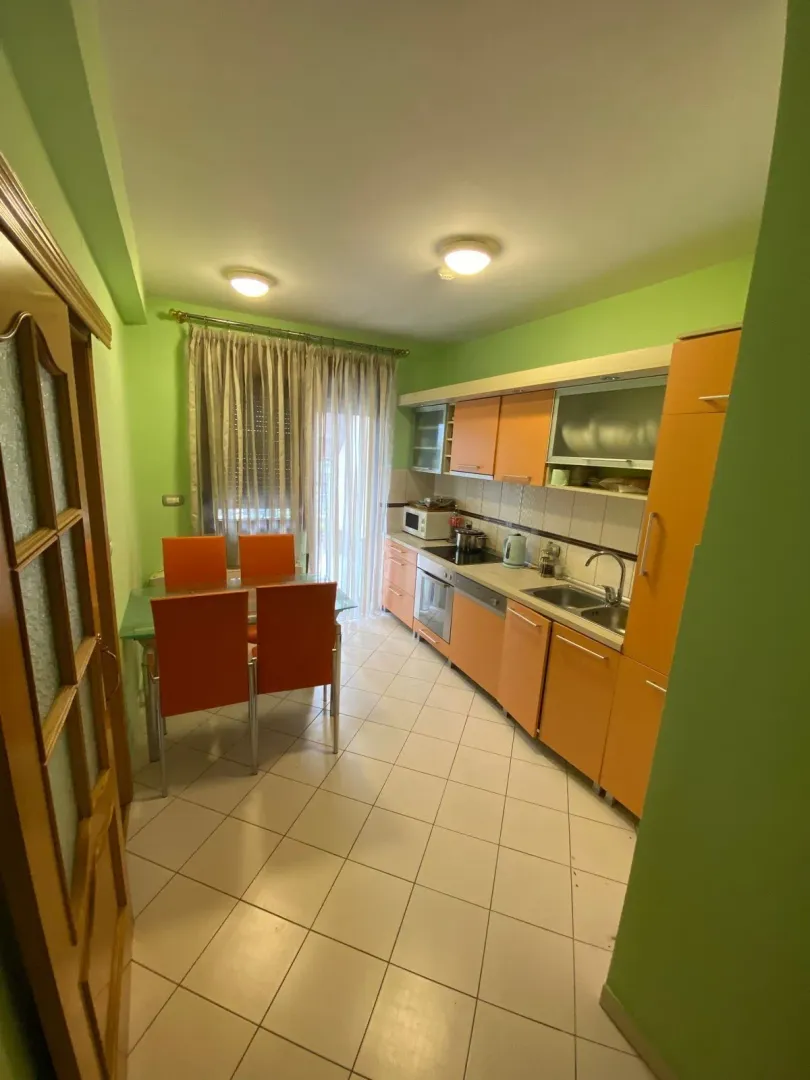 Svijetla kuhinja sa narandžastim elementima i trpezarijskim stolom.