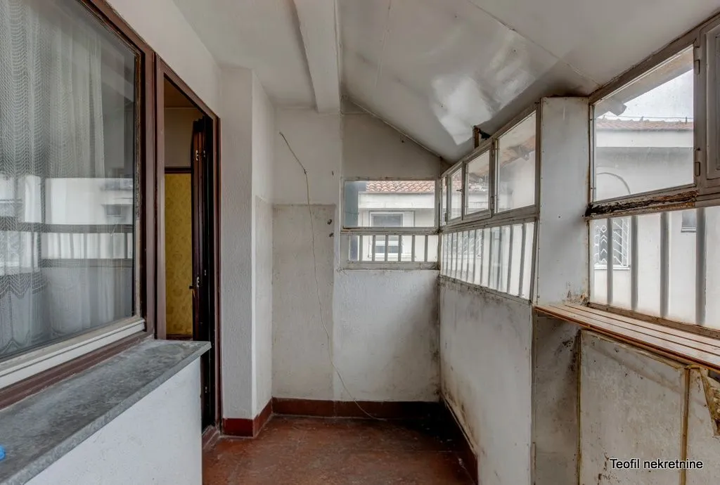 Zastakljeni balkon sa starom stolarijom i pogledom na okolne zgrade.