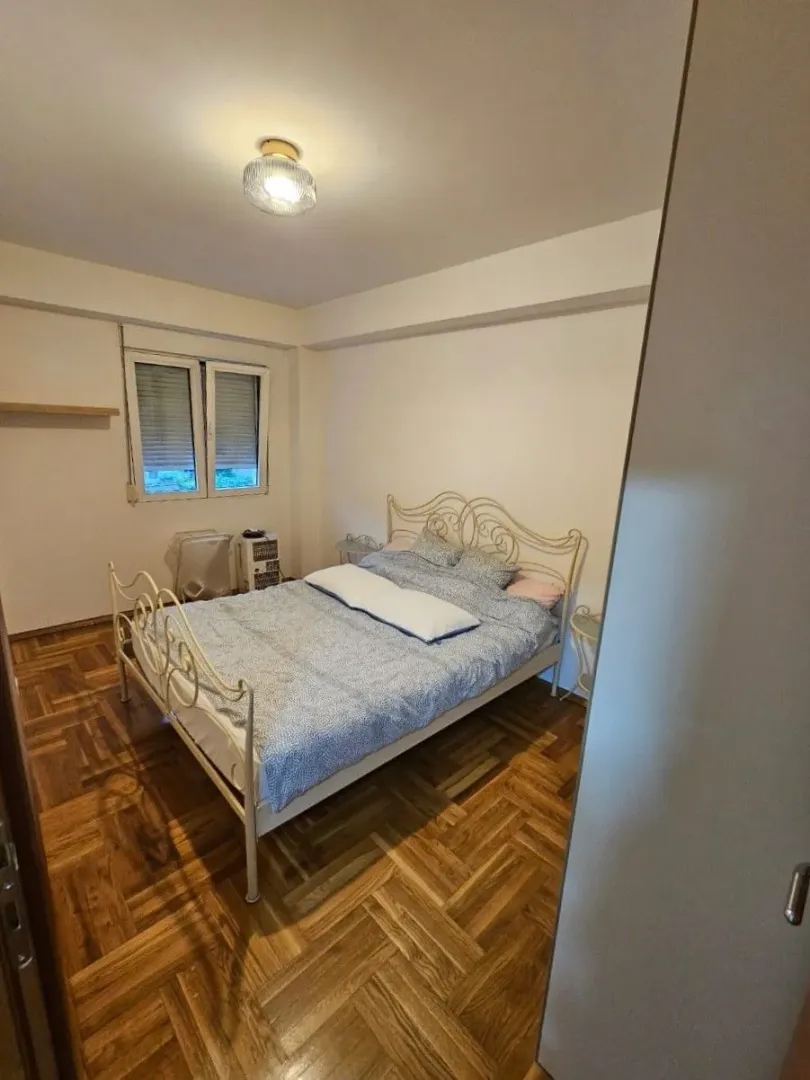 Spavaća soba sa bračnim krevetom, parketom i prozorom.