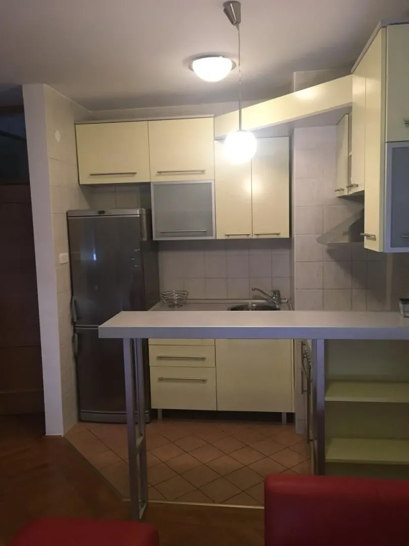 Kuhinja sa svijetlim kuhinjskim elementima, frižiderom i šankom.